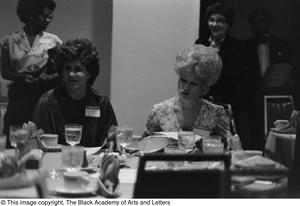 [Two unidentified women seated and chatting at a dining table]