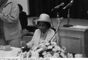 [Photograph of woman seated beside podium]