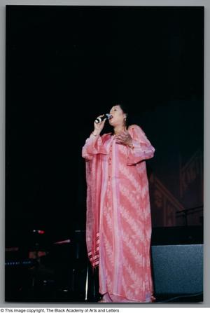 [Full body shot of Angela Bofill singing onstage in a pink dress]