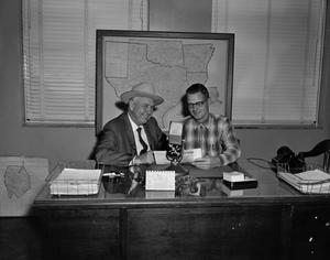 [Calvin Pigg and an unidentified man sitting at a desk]