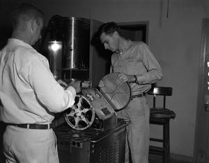 [Two men working with film equipment]