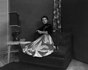 [Photograph of Ann Alden sitting on a patterned couch]