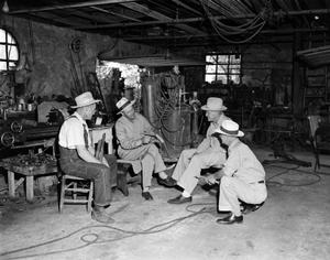 [Photograph of four men in a blacksmith shop]