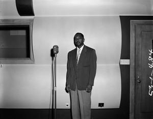 [Photograph of unidentified man stands in front of microphone]