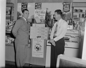 [Men standing by a Fatima Cigarettes display in a store]
