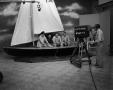 Photograph: [Men sitting in a sailboat on set]