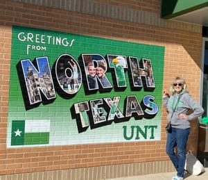 [Alumna with "Greetings from North Texas" Mural]