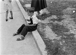 [Photograph of a boy sitting on a curb]