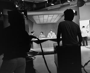 [Photo of camera operators silhouette filming news team]