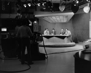 [Photograph of newsmen and floor crew silhouette]