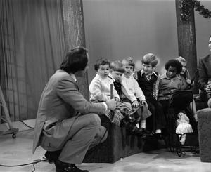 [Photograph of Bill Kelley kneeling next to a group of children at a KXAS Christmas Children's Hour party]