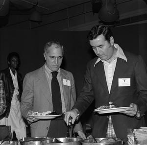 [Photograph of two men fixing plates of food at a buffet]
