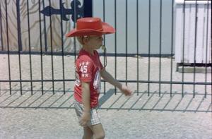 [Young boy wearing a red cowboy hat and walking]