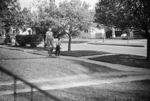 [Photograph of a man and a young boy in a neighborhood]