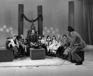 [Photograph of Bill Kelley speaking into a microphone at a KXAS Christmas Children's Hour party]