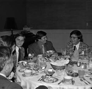 [Photograph of five men dining at an event]