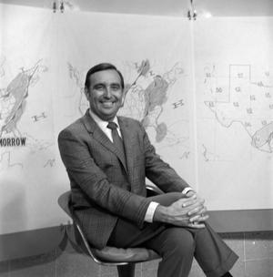 [Ron Godby sitting in front of weather maps]