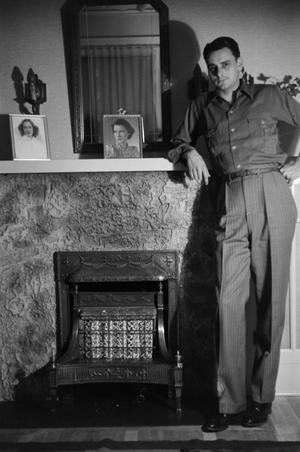 [Photograph of a man posing by a fireplace]