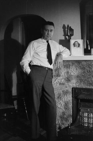 Photograph of a man standing next to a fireplace]