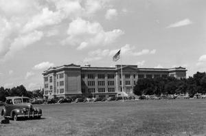 [Photograph of automobiles parked outside a large building]