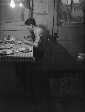 [Photograph of a man eating in a dining room]