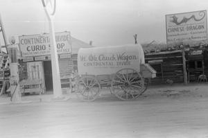 [A covered wagon in front of shops]