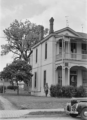 [Photograph of a man standing outside a large house]