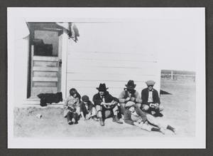 [Photograph of individuals in hats sitting outside a house]