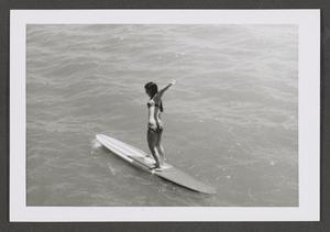 [Photograph of a woman standing on a surfboard]