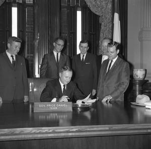 [Texas Governor Price Daniel signing paperwork with people behind him]