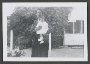[Photograph of a woman holding a baby outside]