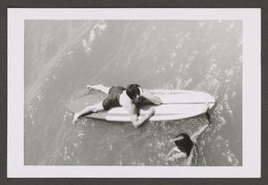[Photograph of a teenage boy on a surfboard and a girl swimming next to him]