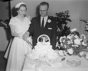 [Photograph of a bride and groom cutting their wedding cake]