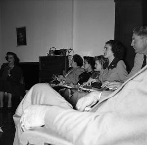 [Photograph of individuals sitting in a row in a room]
