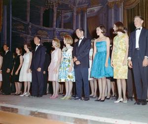 [Group of men and women in formal attire standing side-by-side on stage]
