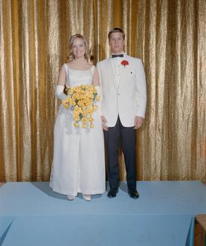[Man and woman in formal attire posing in front of a curtain backdrop]