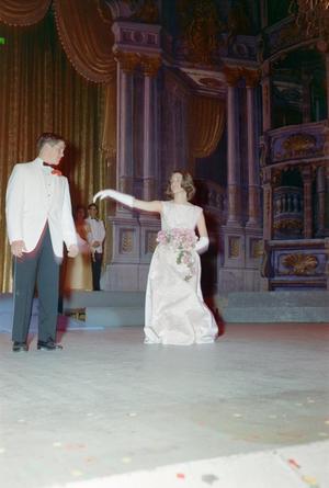 [Man and woman dancing on a stage, dressed in formal attire, woman holds bouquet]