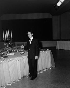 [Man in formal attire standing next to a table of food]