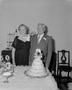 Photograph: [Older man and woman standing side-by-side behind a cake]