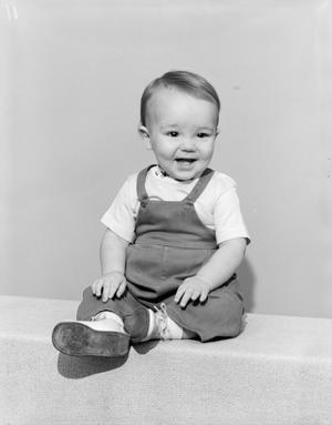 [Photograph of toddler boy in overalls, boots and a short-sleeve shirt, smiling]