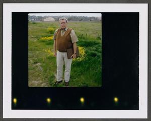 [Man standing in a field with houses in the background]