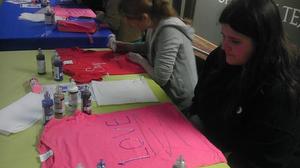 [Student decorating red and pink Clothesline Project t-shirts]