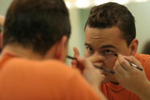 [Photograph of a man applying eyeliner in mirror]