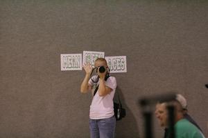 [Woman holds camera in front of "Mean Green Aces" sign]