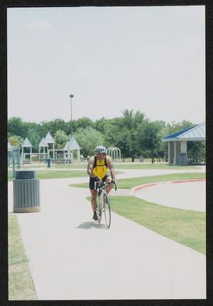 [Cyclist in yellow riding along a park path: Lone Star Ride 2003 event photo]