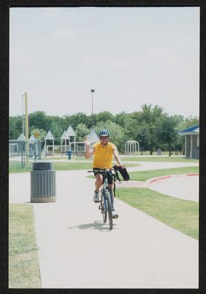 [Cyclist in yellow waving as he rides in: Lone Star Ride 2003 event photo]
