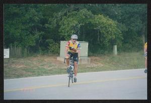 [Cyclist in a red, blue and yellow jersey biking into a campground: Lone Star Ride 2003 event photo]