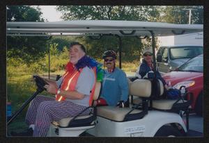 [Man driving a golf cart with two passengers: Lone Star Ride 2003 event photo]