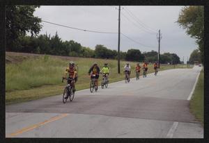 [A line of cyclists biking down a road parallel to railroad tracks: Lone Star Ride event photo]