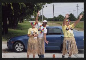 [Three crew members in grass skirts smiling and waving their arms: Lone Star Ride event photo]